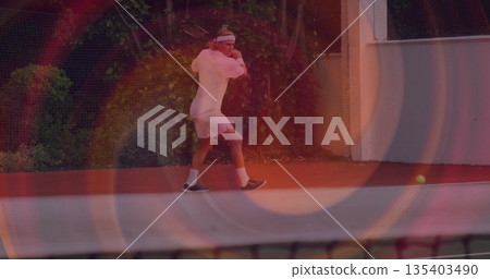 Swinging male tennis player hitting backhand on red hardcourt, with racquet headband ball net Swinging male tennis player hitting backhand on red hardcourt, with racquet headband ball net 135403490