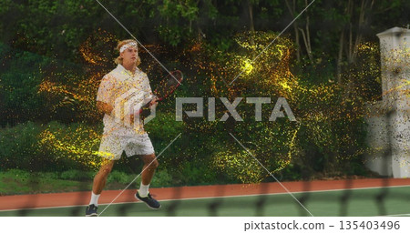Positioning male tennis player gripping racket behind net on court, with swirling golden particles 135403496