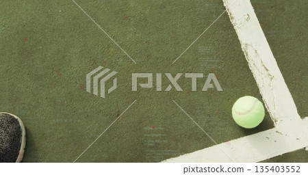Tennis ball resting in corner of green court near white lines, with athletic sneaker, copy space 135403552