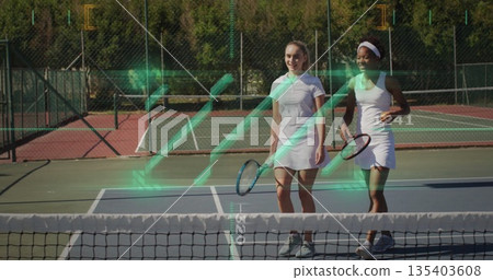 Walking partners in white dresses holding rackets on tennis court with net, fence and AR overlay 135403608