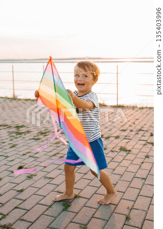 Joyful Boy Playing With Colorful Kite At Sunset 135403996