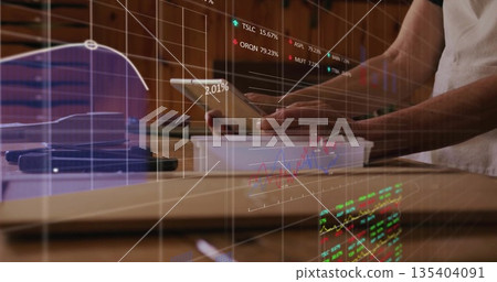 Reviewing financial charts while holding tablet above plastic tray at wooden kitchen counter 135404091