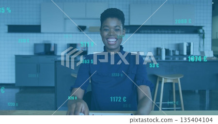 Smiling woman wearing dark blue blouse typing at table in office break room, with financial overlay Smiling woman wearing dark blue blouse typing at table in office break room, with financial overlay 135404104