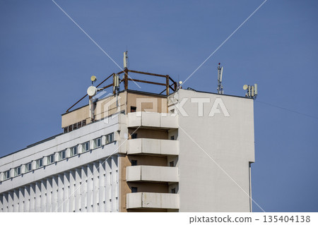 Rooftop features multiple telecommunication antennas placed on a tall building in a city setting in bright daylight 135404138