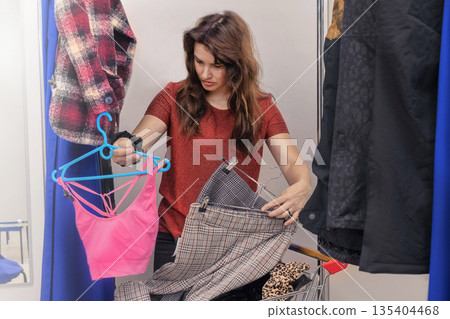 Caucasian woman walks around the store, shopping. Woman in fitting room going to measure clothes, trousers, top close up Caucasian woman walks around the store, shopping. Woman in fitting room going to measure clothes, trousers, top close up 135404468