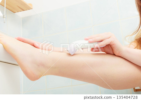Woman shaving legs with depilator in bathroom Woman shaving legs with depilator in bathroom 135404728