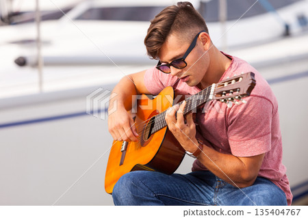 Young guitarist sitting on pier. 135404767