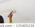 A painter applying fresh white paint to an exterior wall with a roller. 135405238