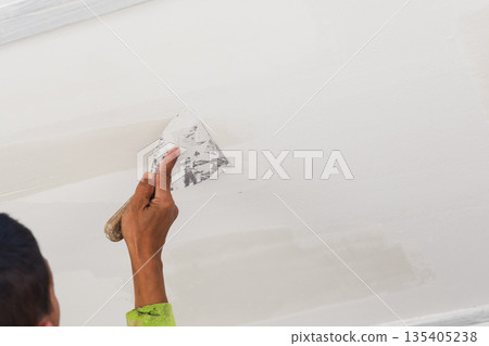 A painter applying fresh white paint to an exterior wall with a roller. A painter applying fresh white paint to an exterior wall with a roller. 135405238