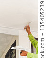 Vertical worker applying plaster with a putty knife on a ceiling surface. 135405239