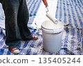 A painter dipping a roller into a bucket of white paint during an interior renovation. 135405244
