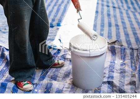 A painter dipping a roller into a bucket of white paint during an interior renovation. 135405244
