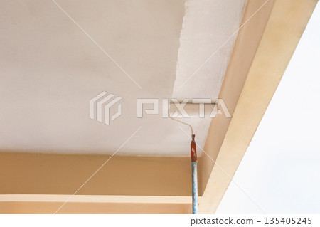 Painter using a roller to apply fresh white paint to a ceiling. Painter using a roller to apply fresh white paint to a ceiling. 135405245