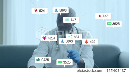 Gesturing doctor in white coat with stethoscope and blue latex gloves at clinic showing media icons 135405487