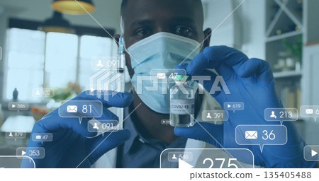 Holding masked researcher inspecting COVID-19 vaccine vial in laboratory, with notification icons 135405488