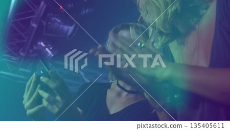 Scrolling smartphone by woman wearing choker and friend at club under truss haze spotlights 135405611