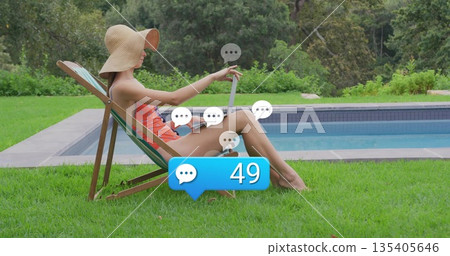 Reclining woman wearing orange swimsuit and straw hat reaching for tablet by pool with alerts Reclining woman wearing orange swimsuit and straw hat reaching for tablet by pool with alerts 135405646