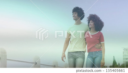 Walking couple wearing T-shirt and jeans strolling along waterfront promenade with metal railing Walking couple wearing T-shirt and jeans strolling along waterfront promenade with metal railing 135405661