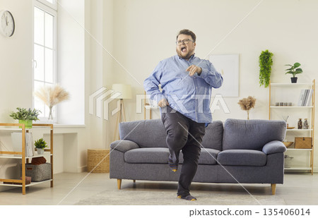Happy overweight man kicking while dancing on sofa in modern living room Happy overweight man kicking while dancing on sofa in modern living room 135406014