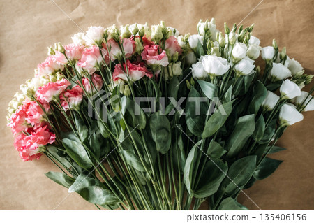 Bunches of pink and white lisianthus flowers lie flat on brown paper. Eryngium alpium, goldenrod, floristry workshop, slow living, hand-gathered bouquets. Bunches of pink and white lisianthus flowers lie flat on brown paper. Eryngium alpium, goldenrod, floristry workshop, slow living, hand-gathered bouquets. 135406156