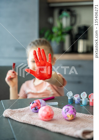 Little girl painting her hand with red paint while decorating Easter eggs at home. Creative Easter activity, childhood curiosity and playful holiday preparation indoors. Little girl painting her hand with red paint while decorating Easter eggs at home. Creative Easter activity, childhood curiosity and playful holiday preparation indoors. 135406271