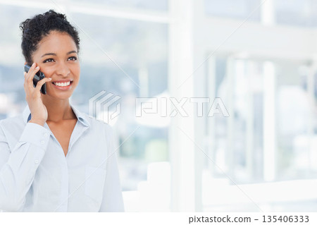 African American woman wearing blue shirt talking on smartphone by office glass panels, copy space 135406333