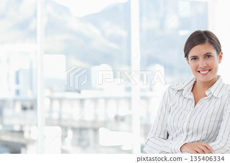 Female professional smiling while sitting in office chair at desk with glass windows, copy space Female professional smiling while sitting in office chair at desk with glass windows, copy space 135406334