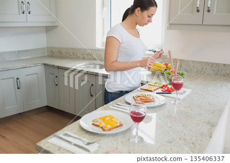 Woman standing at marble countertop in home kitchen, assembling toast and pouring juice, copy space Woman standing at marble countertop in home kitchen, assembling toast and pouring juice, copy space 135406337
