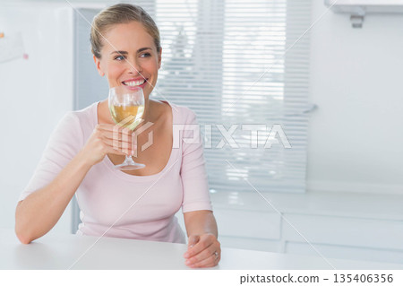 Woman in her 30s wearing pink top sitting at modern kitchen counter holding wine glass smiling Woman in her 30s wearing pink top sitting at modern kitchen counter holding wine glass smiling 135406356