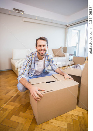 Male crouching on parquet floor in living room opening large cardboard box beside sliding door Male crouching on parquet floor in living room opening large cardboard box beside sliding door 135406384