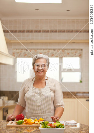 Senior woman chopping bell peppers on wooden cutting board at marble countertop island in kitchen Senior woman chopping bell peppers on wooden cutting board at marble countertop island in kitchen 135406385