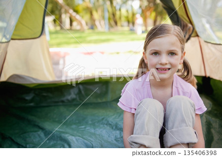 School-age girl sitting inside open dome tent with green groundsheet tarp on park lawn, copy space 135406398