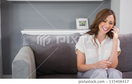 Woman smiling and talking on smartphone while sitting on grey sofa at home, copy space Woman smiling and talking on smartphone while sitting on grey sofa at home, copy space 135406417