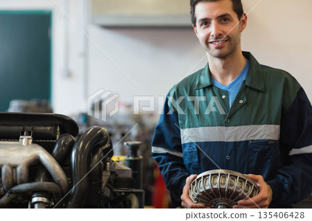 Male mechanic wearing coverall holding converter beside car engine stand in workshop, copy space 135406428