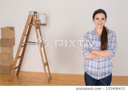 Woman standing with arms crossed in room under renovation with ladder, paint can, boxes, copy space Woman standing with arms crossed in room under renovation with ladder, paint can, boxes, copy space 135406433