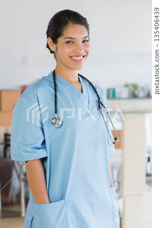 Mid-adult female clinician standing in clinic wearing blue scrubs and holding stethoscope 135406439