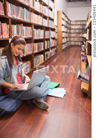 Woman sitting in library aisle working on laptop with notebooks, folder and backpack, copy space Woman sitting in library aisle working on laptop with notebooks, folder and backpack, copy space 135406441
