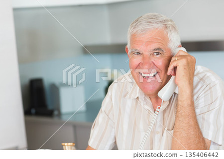 Senior man sitting at kitchen table talking on landline phone with ceramic mug, copy space Senior man sitting at kitchen table talking on landline phone with ceramic mug, copy space 135406442