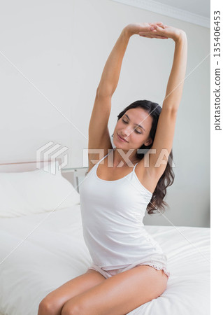 Woman stretching arms overhead on bed in bright bedroom with white duvet and pillows Woman stretching arms overhead on bed in bright bedroom with white duvet and pillows 135406453
