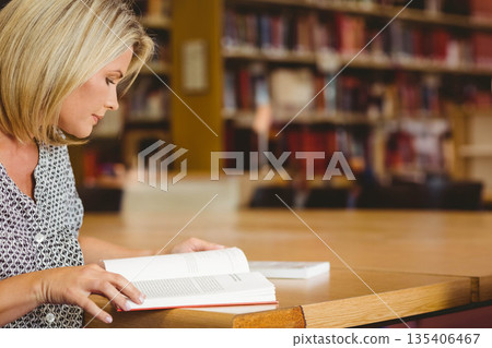 Woman reading open book and turning pages at library reading room wooden table, copy space 135406467