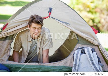 Man leaning out of tent entrance at grassy campground, showing dome tent and camping backpack Man leaning out of tent entrance at grassy campground, showing dome tent and camping backpack 135406475