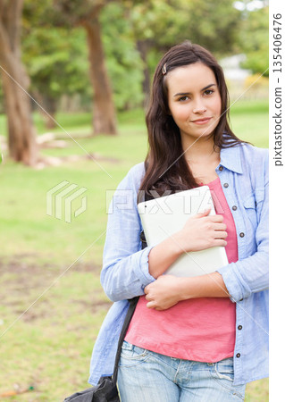 Woman holding digital tablet and wearing denim shirt, carrying shoulder bag in park, copy space 135406476