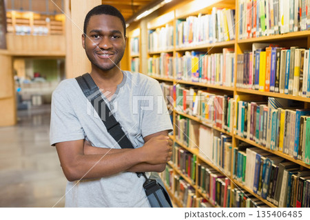 African American adult male crossing arms smiling in library aisle with messenger bag, copy space 135406485
