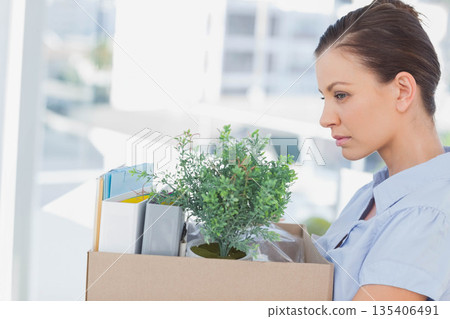 Woman wearing blue shirt holding box with plant, binders, folders in modern office, copy space 135406491