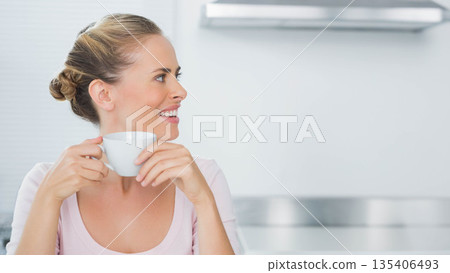 Mid adult woman standing in modern kitchen holding white mug near stainless range hood, copy space 135406493