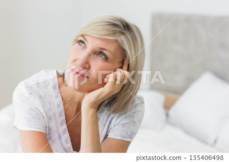 Senior woman resting head on hand and gazing upward in bedroom with white bedding showing ring Senior woman resting head on hand and gazing upward in bedroom with white bedding showing ring 135406498
