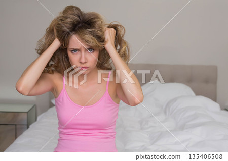 Female pulling hair on bed in bedroom by mirrored nightstand white bedding beige headboard 135406508