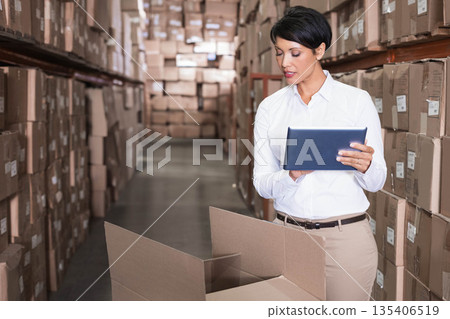 Hispanic mature adult woman holding tablet and reading box label in warehouse managing inventory Hispanic mature adult woman holding tablet and reading box label in warehouse managing inventory 135406519