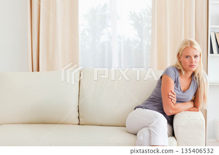 Woman sitting on sofa arm holding arms near window and shelving in living room, copy space Woman sitting on sofa arm holding arms near window and shelving in living room, copy space 135406532