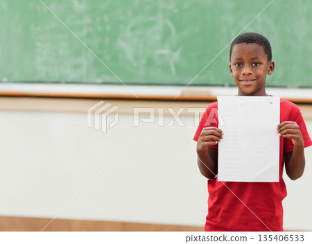 African American boy holding test paper and smiling in classroom by green chalkboard, copy space African American boy holding test paper and smiling in classroom by green chalkboard, copy space 135406533